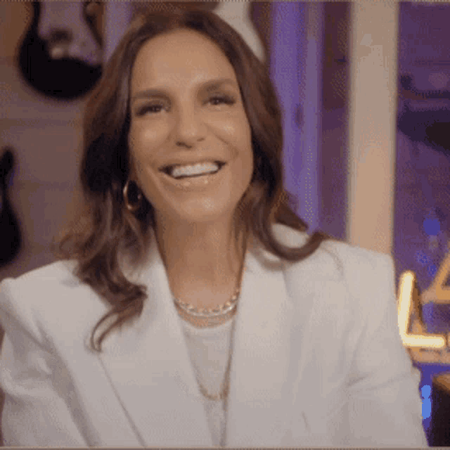 a woman is wearing a white jacket and a necklace and smiling .