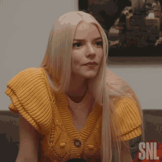 a woman wearing a yellow sweater with the letters snl on the bottom right
