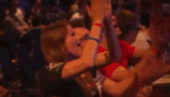 a group of people are sitting in a dark room with their arms up in the air .