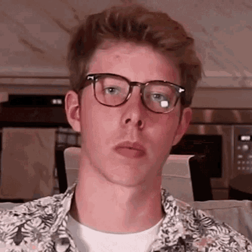 a young man wearing glasses and a shirt is making a funny face .