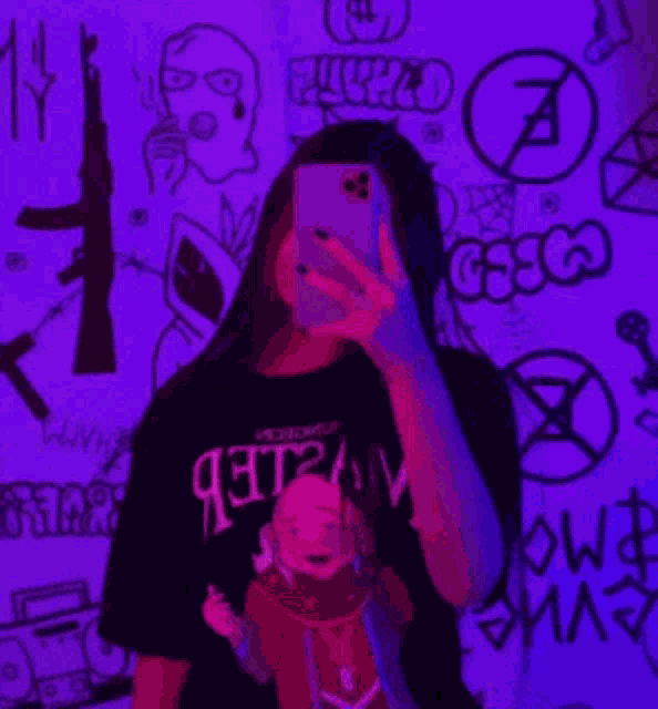 a woman is taking a selfie with her phone in front of a purple wall with drawings on it .