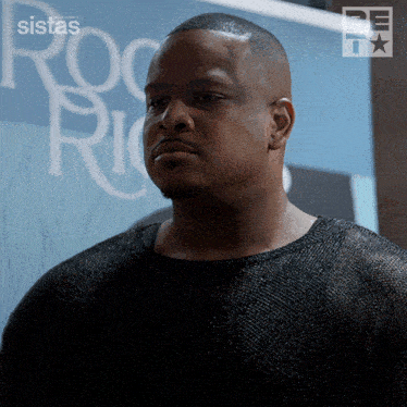 a man stands in front of a sign that says ' sistas ' on it