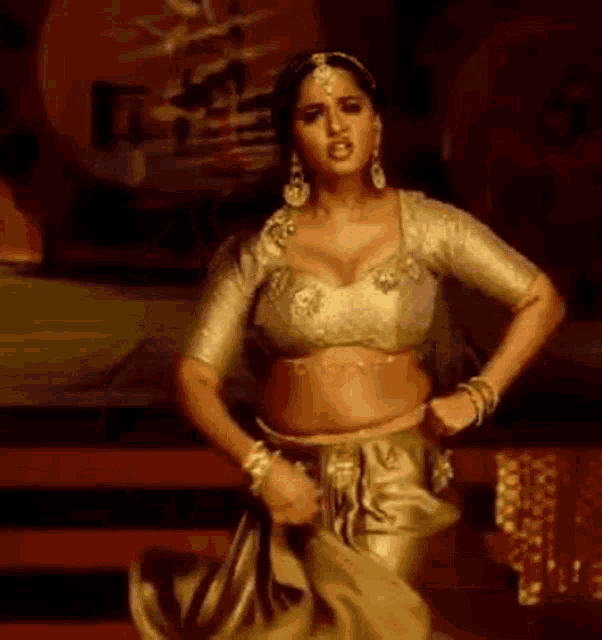 a woman in a crop top and a gold skirt is dancing on a stage .