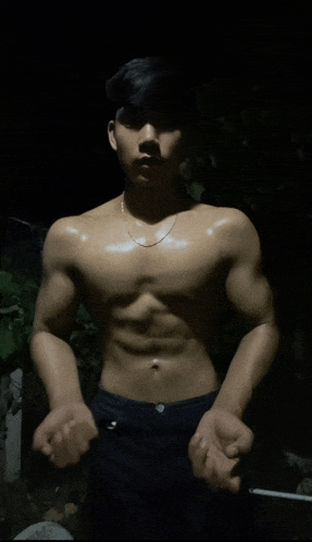 a shirtless man with a chain around his neck stands in the dark