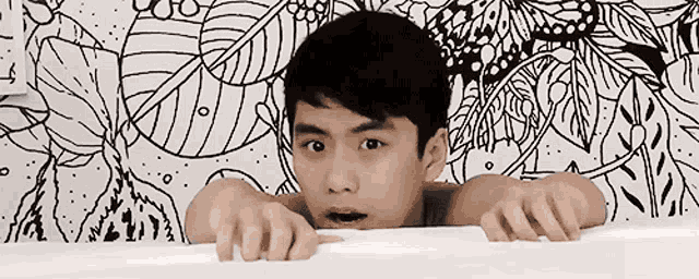 a young man is peeking over the edge of a bathtub in front of a black and white drawing on the wall