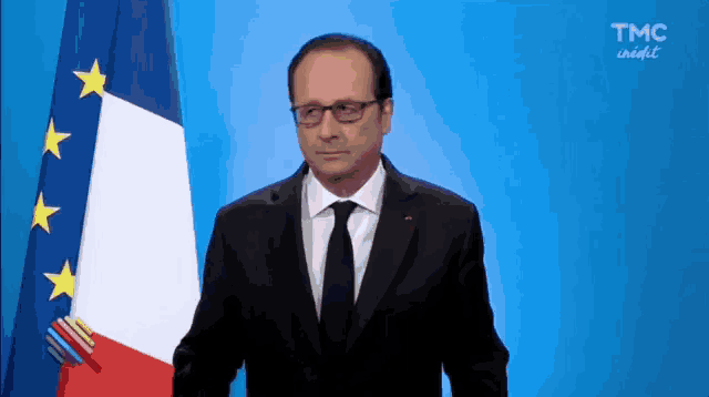 a man in a suit and tie is standing in front of a french flag