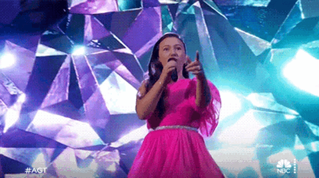a girl in a pink dress is singing into a microphone on stage .