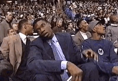 a man in a suit and tie is sitting in front of a crowd of people at a basketball game .