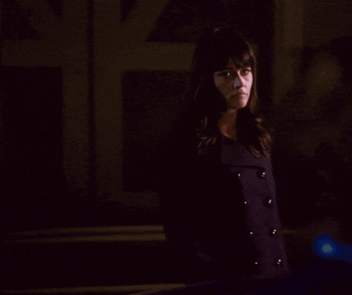 a woman in a dark room is looking at the camera with a serious look on her face
