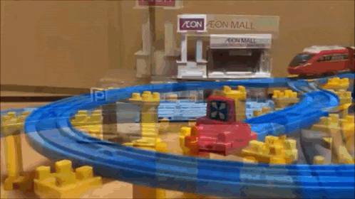 a toy train is going around a track in front of a aeon mall