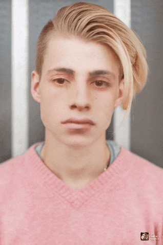 a young man with blonde hair is wearing a pink sweater with a bear on it