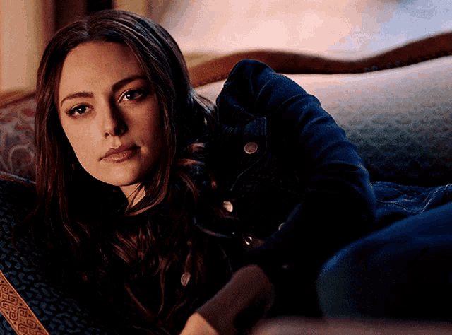 a woman in a denim jacket is laying on a couch looking at the camera