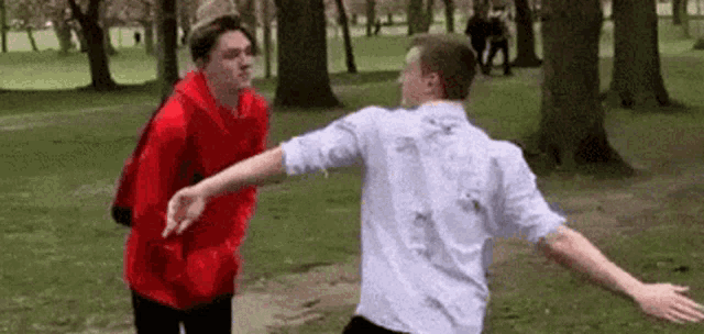 two men are standing next to each other in a park and hugging each other .