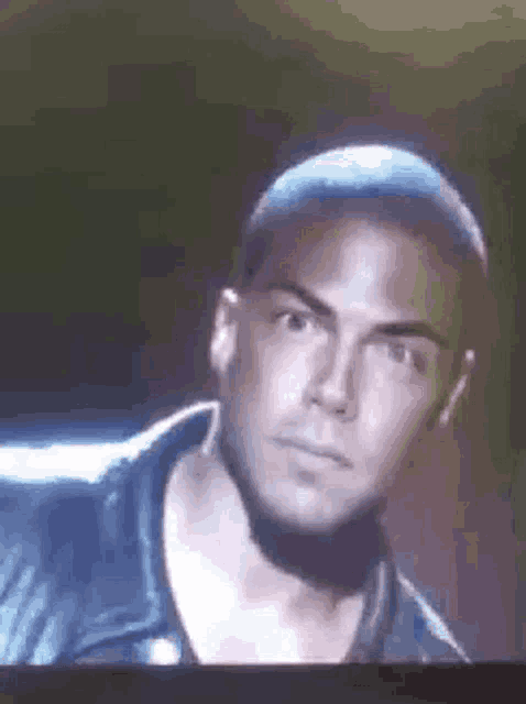 a man with a shaved head is looking at the camera on a television screen .