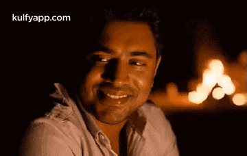 a man is smiling in front of a fire and the website kulfyapp.com is visible in the corner .