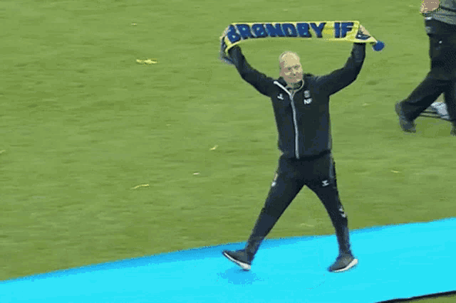 a man holds up a blue and yellow scarf that says brandby ifl