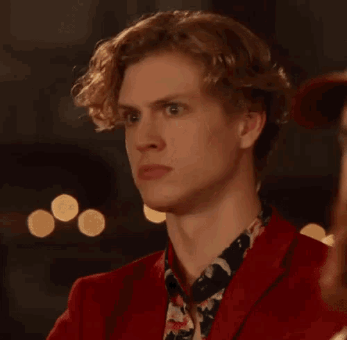a young man wearing a red jacket and a floral shirt is looking at the camera .