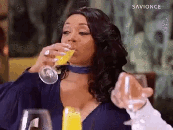 a woman is drinking a glass of orange juice at a table .