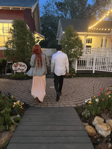 a man and woman are walking towards a rose cottage sign
