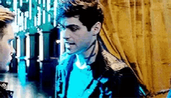 a man in a leather jacket is standing next to another man in a blue shirt .