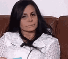 a woman is sitting on a couch with a bag on her lap and looking at the camera .