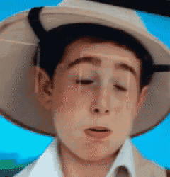 a boy wearing a hat and a white shirt is making a sad face