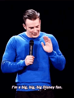 a man in a blue sweater holds a microphone and says i 'm a big big big disney fan