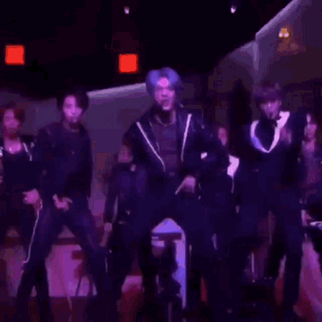 a man with blue hair is dancing in a dark room while another man looks on .