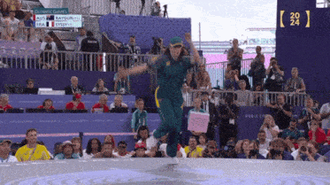 a woman in a green outfit is jumping in front of a crowd at the olympics