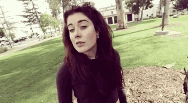 a woman is standing in a park wearing sunglasses and a black shirt .