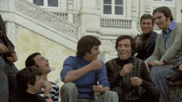 a group of men are laughing together in front of a building with a balcony