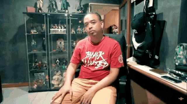 a man wearing a red shirt with the word black on it is sitting in a chair