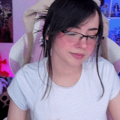 a woman wearing glasses and a white shirt is sitting in a chair and looking at the camera .