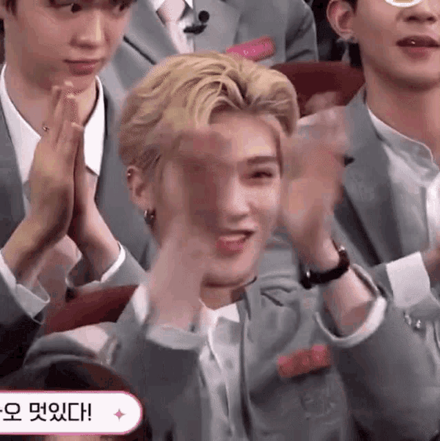 a man in a suit is clapping his hands while sitting in a crowd .