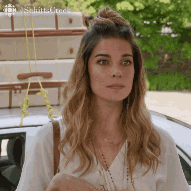 a woman is standing in front of a car with luggage on the roof and #schittscreek written on the bottom