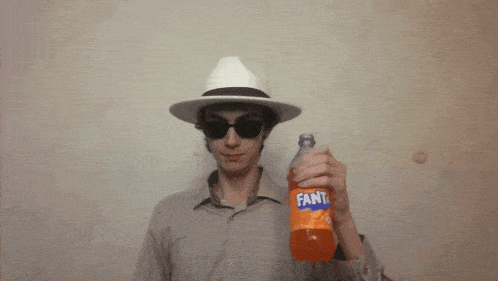 a man wearing a hat and sunglasses holds up a bottle of fanta