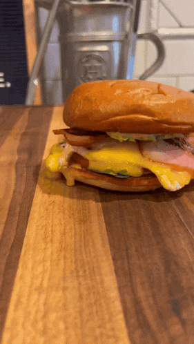 a sandwich on a wooden cutting board with a cup in the background