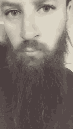 a man with a beard is taking a selfie with his camera .