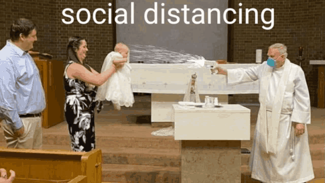 a priest wearing a mask is spraying water on a baby during a baptism