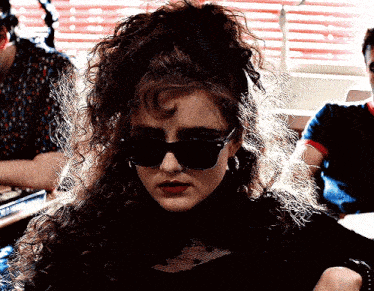 a woman with curly hair wearing sunglasses and earrings is sitting in front of a window .