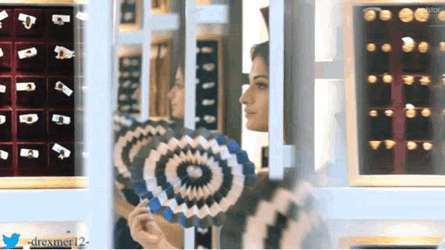 a woman is holding a fan in front of a display of jewelry with the twitter username drexmer12 at the bottom
