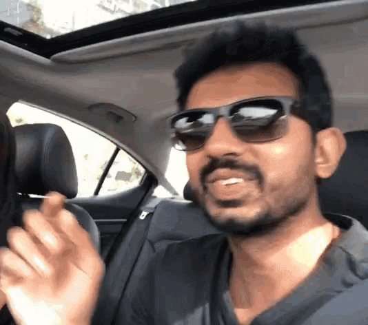 a man with a beard wearing sunglasses is in the back seat of a car