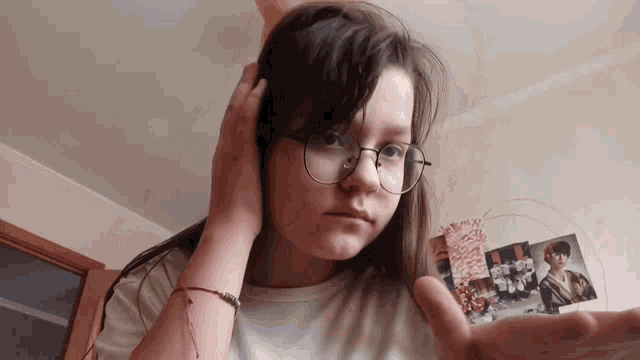 a girl wearing glasses holds her hand out in front of a wall with pictures on it