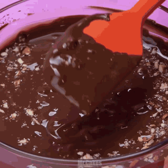 a spatula is being used to stir a bowl of chocolate sauce with nuts