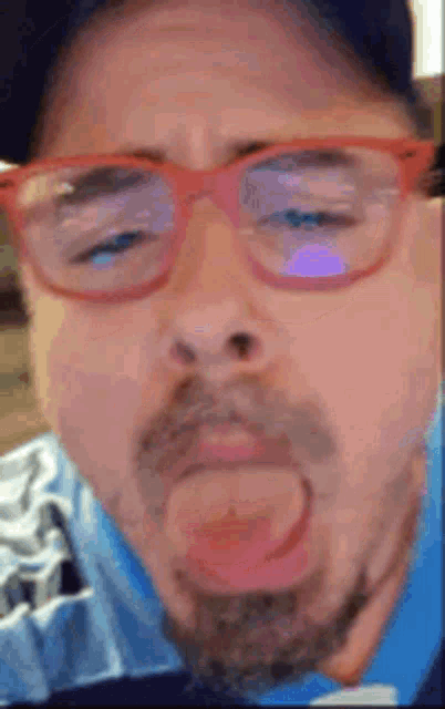 a man wearing red glasses and a hat is sticking his tongue out .