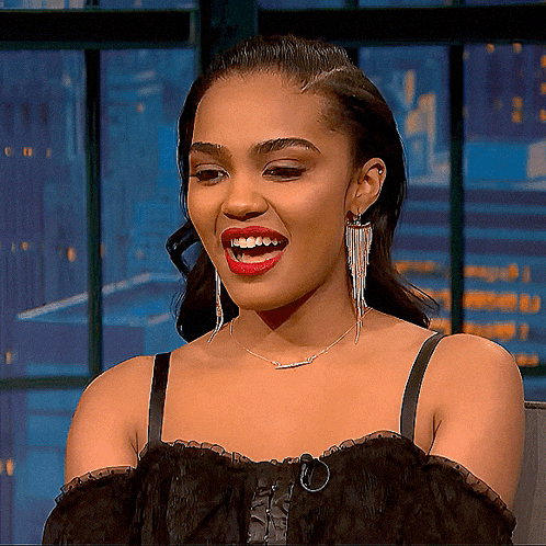 a woman wearing a black top and earrings smiles