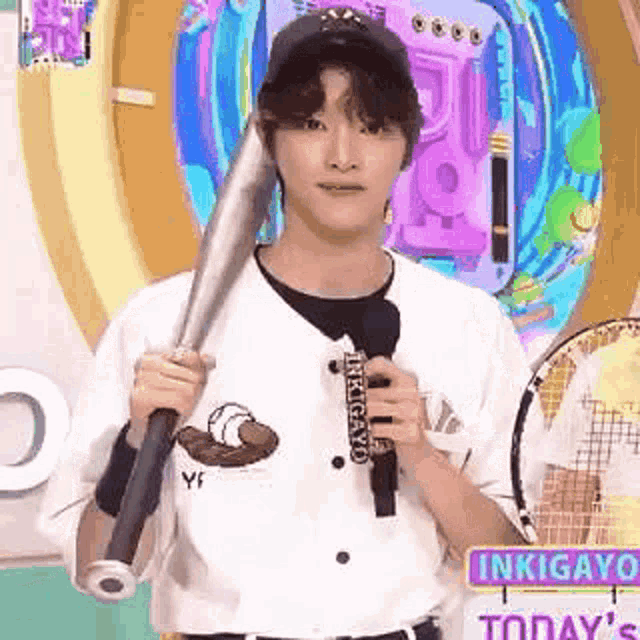 a young man in a baseball uniform is holding a baseball bat and a tennis racquet .