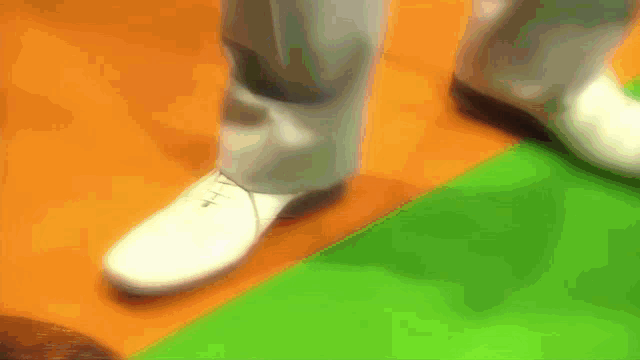 a person wearing white shoes is standing on a green and orange carpet