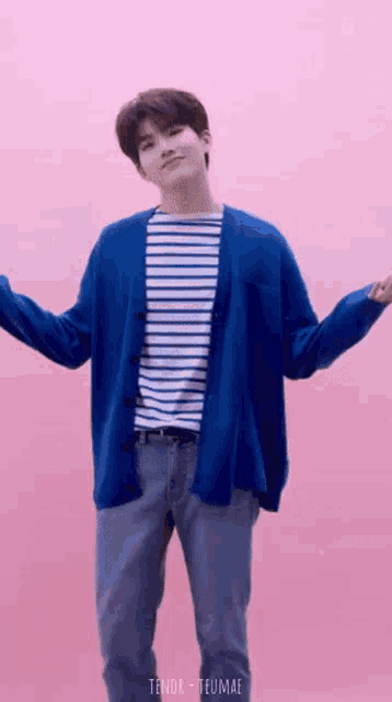 a man wearing a blue cardigan and a striped shirt is standing in front of a pink background .