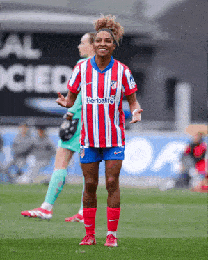 a female soccer player wearing a red and white striped shirt with the word herbalife on it
